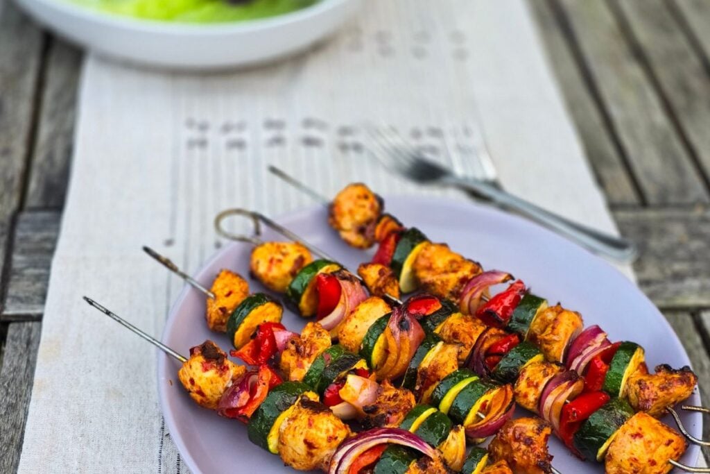 five skewers of harissa marinated chicken with zucchini peppers and red onion served on a lilac plate