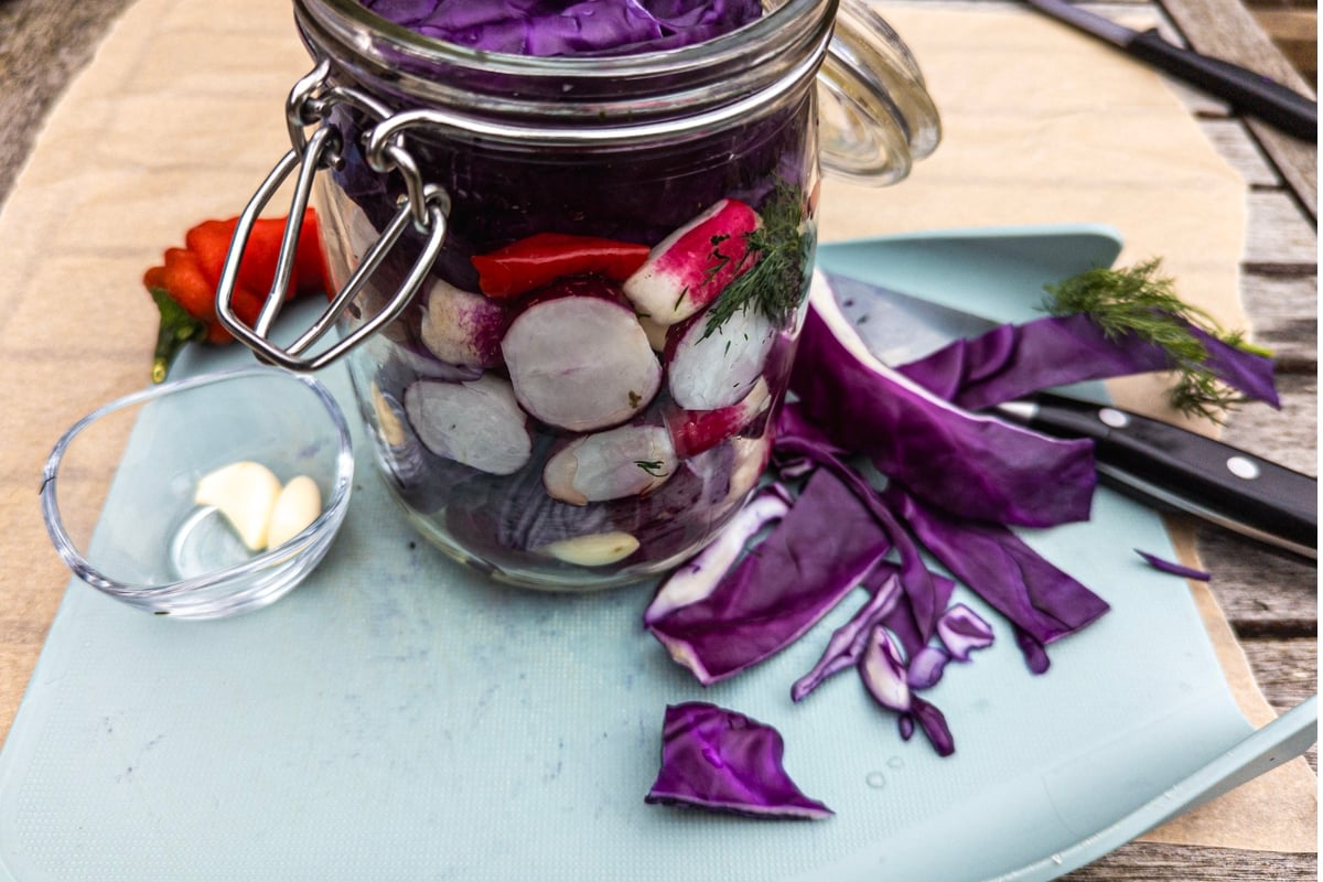 Red cabbage slices on blue chopping board and radishes in a jar