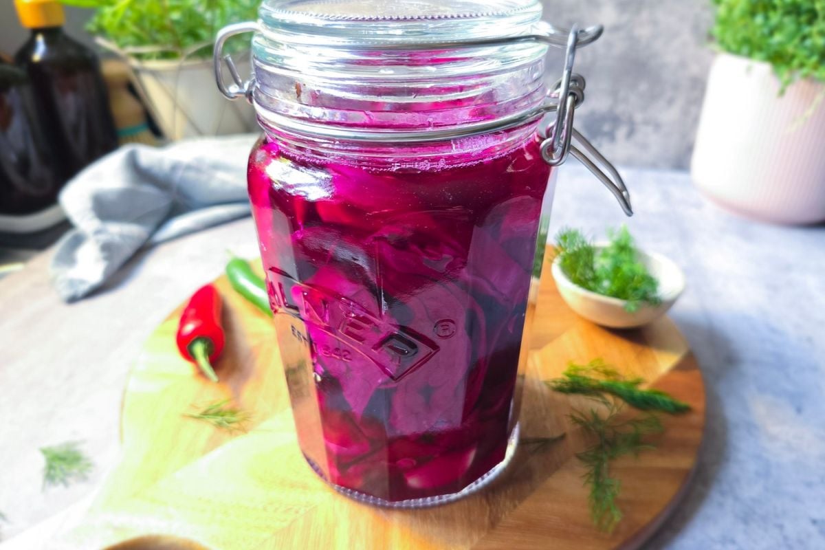 Jar of pink sauerkraut after a week of fermenting, the brine turned bright pink, with chilies and dill on a wooden board.