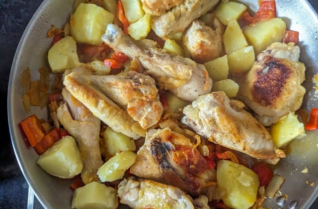 Chicken pieces stewing with sauteed veggies in frying pan