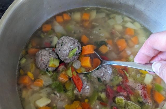 Meatballs cooking in a chunky vegetable broth