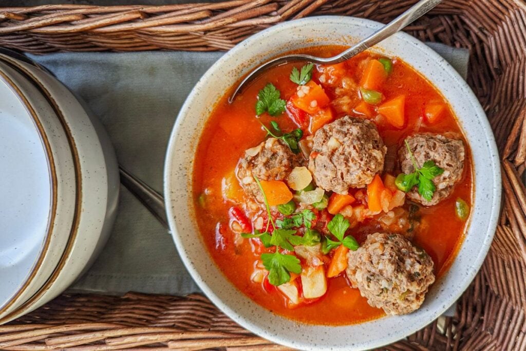 A tomato and vegetable soup with meatballs in a white bowl