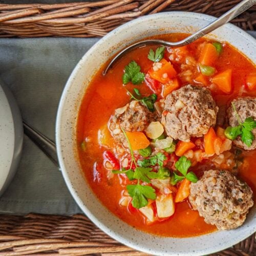 A tomato and vegetable soup with meatballs in a white bowl