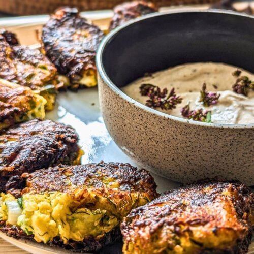 Courgette feta fritters on a white plate with a bowl of tahini yogurt fip