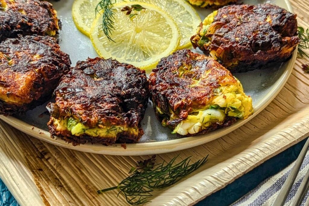 Zucchini feta fritters on a plate with slices of lemon and dill fronds