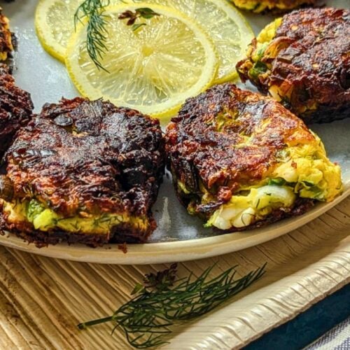 Zucchini feta fritters on a plate with slices of lemon and dill fronds