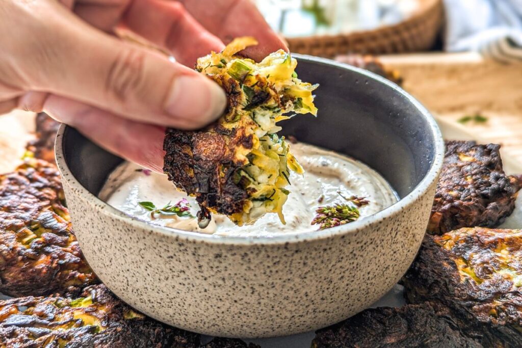 Zucchini and feta fritter being dipped in yogurt dip