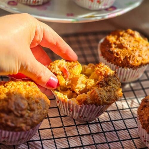 opening up a rhubarb and apple muffing by hand and other muffins on a black cooling grid