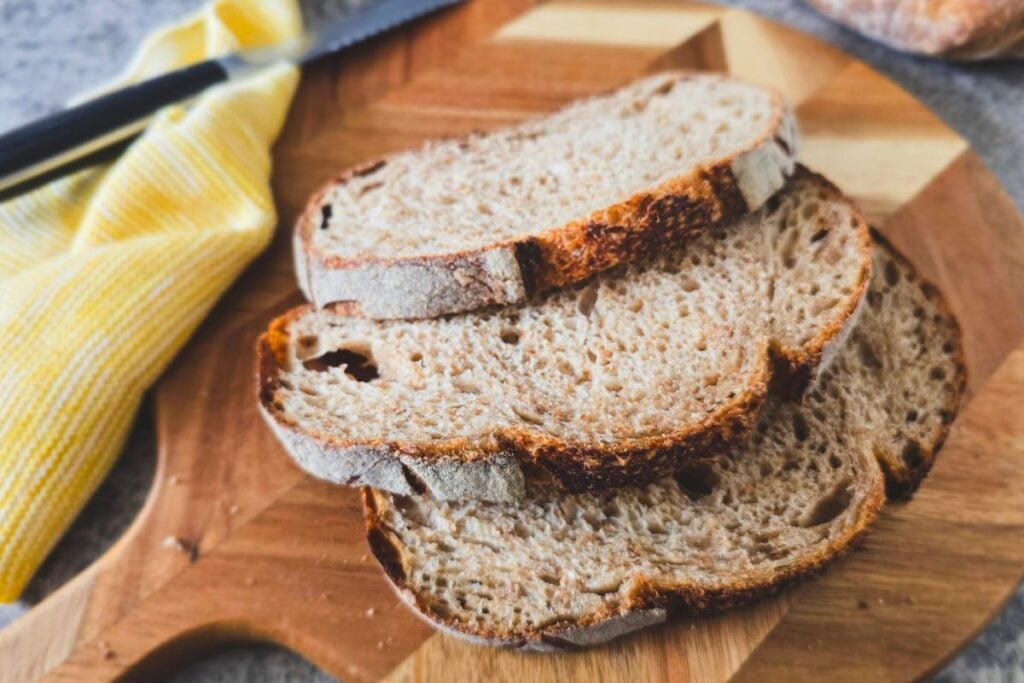 Stack of brown sourdough slices on a board, airy wholemeal crumb with browned crust edges.