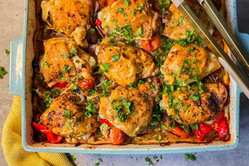 Portuguese-inspired peri peri chicken and rice traybake with peppers, onions, cherry tomatoes and parsley.