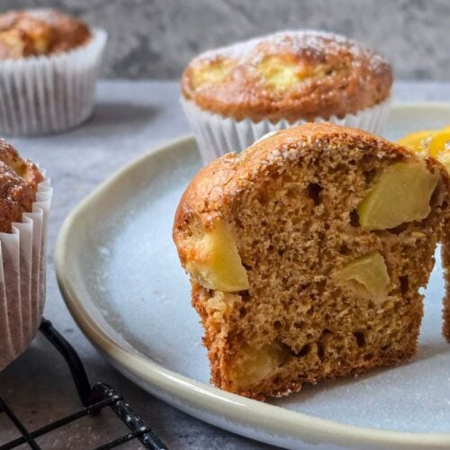 Halved apple sourdough muffin on a plate, showing a tender crumb with diced apple pieces.