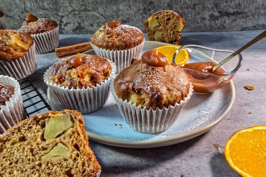 Plate of apple sourdough muffins with a small bowl of apple butter, orange slices and a cinnamon stick.