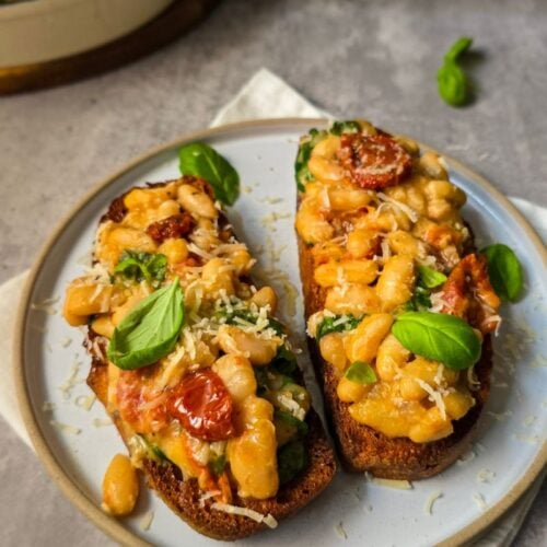 Creamy miso beans with spinach and sundried tomatoes on sourdough toast, topped with fresh basil and parmesan