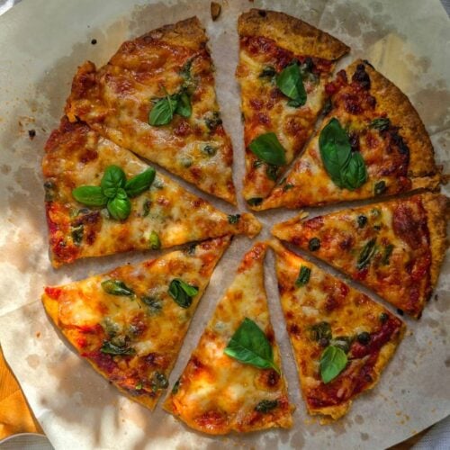 Sliced piadina pizza with marinara, melted mozzarella, capers, and fresh basil on parchment paper.