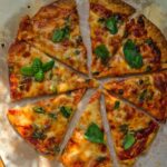Overhead view of sliced piadina pizza on parchment paper, topped with melted mozzarella, capers, and fresh basil.