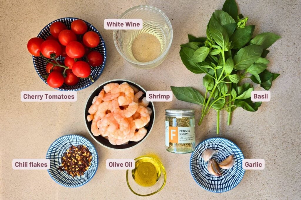 Overhead photo of shrimp marinara ingredients: shrimp, cherry tomatoes, basil, garlic, fennel seeds, olive oil, chili flakes, and white wine.