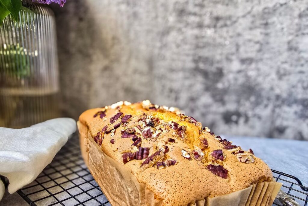 Freshly baked Pan di Spagna loaf cake with toasted pecans cooling on a wire rack.