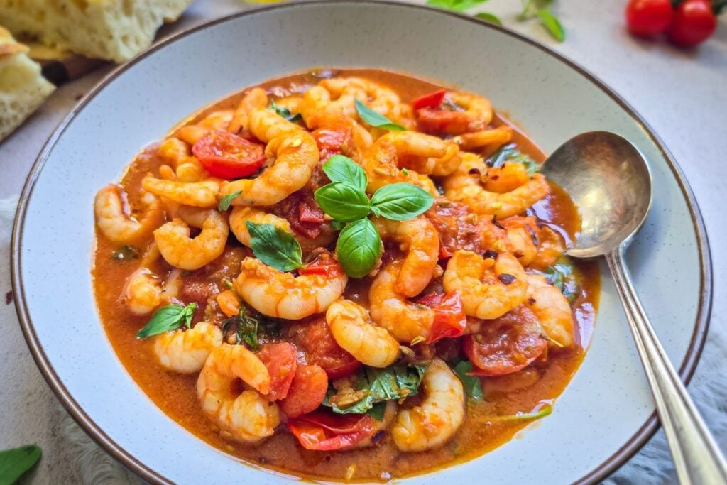 shrimp marinara with cherry tomatoes, basil, and olive-oil in a shallow bowl.