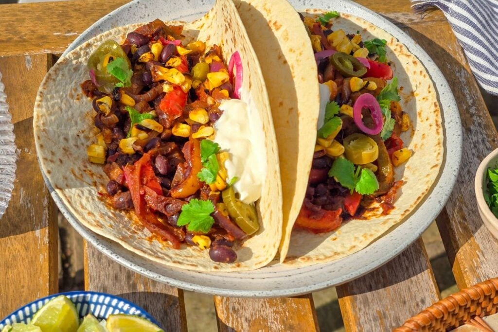 Black bean fajitas served outside in tortillas with charred corn, jalapeños, cilantro, sour cream, and lime.