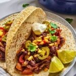 Black bean fajitas served in warm tortillas with peppers, onions, charred corn, jalapeños, sour cream, cilantro, and lime wedges.