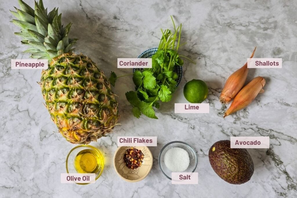 Ingredients for avocado pineapple salsa, including fresh pineapple, avocado, lime, coriander, shallots, chili flakes, salt, and olive oil.