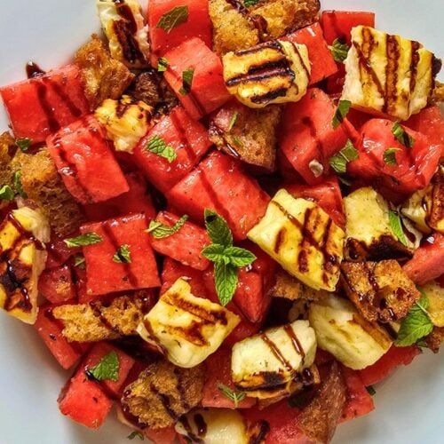 Close-up of watermelon halloumi salad showing juicy watermelon cubes, golden grilled halloumi with char marks, sourdough croutons, fresh mint leaves, and balsamic glaze.