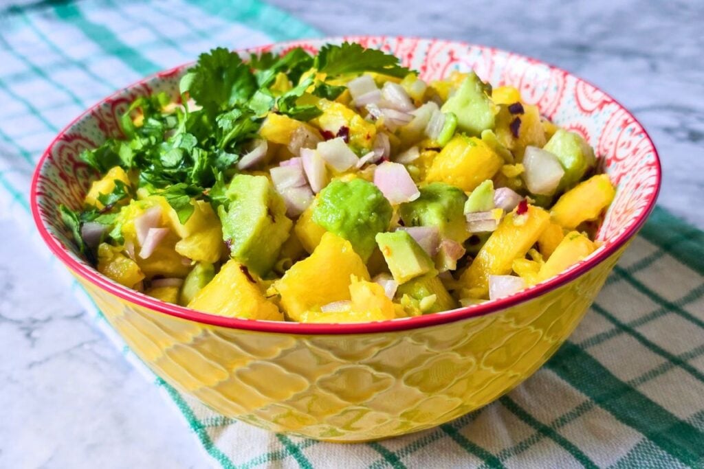 Avocado pineapple salsa in a yellow patterned bowl with fresh coriander, shallot, and chili flakes.