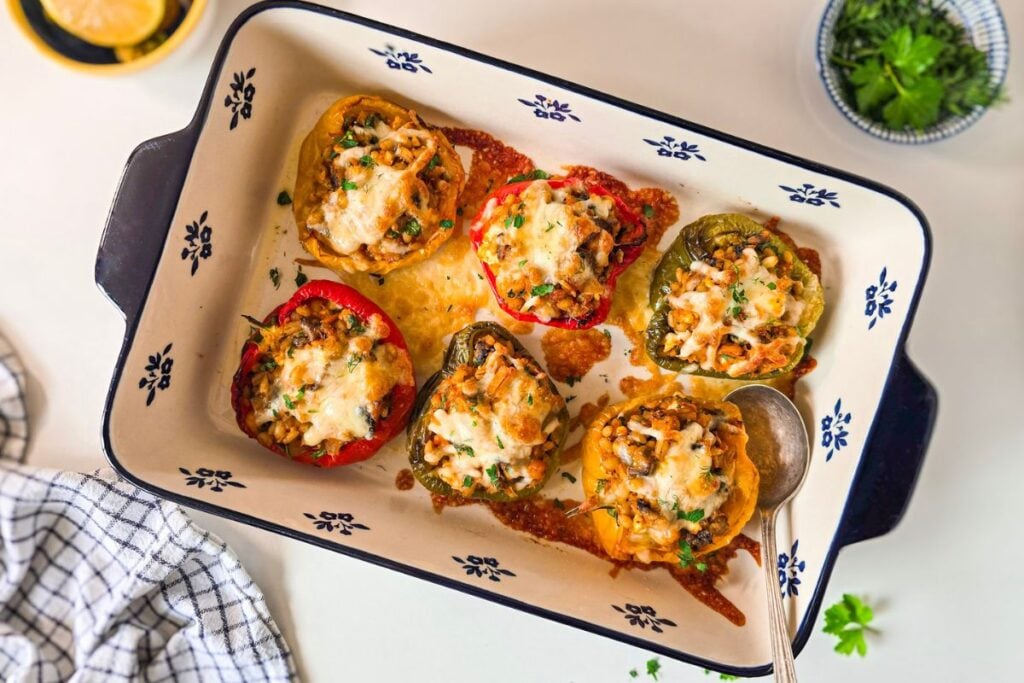 barley stuffed peppers in a blue and white baking dish, topped with melted cheese and fresh herbs.