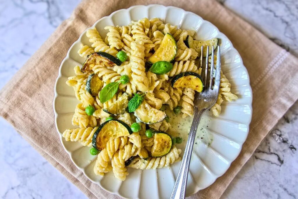 courgette and feta pasta with fusilli, peas, and fresh herbs on a white plate