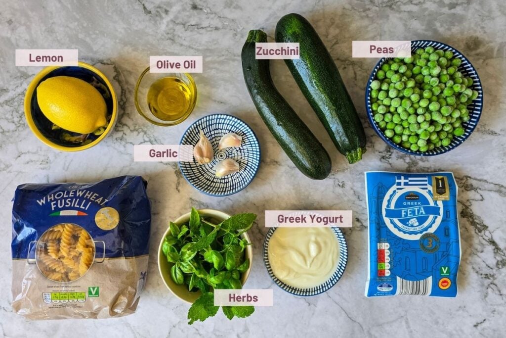 ingredients for zucchini feta pasta: zucchini, feta, Greek yogurt, wholewheat fusilli, frozen peas, garlic, lemon, olive oil, and fresh herbs