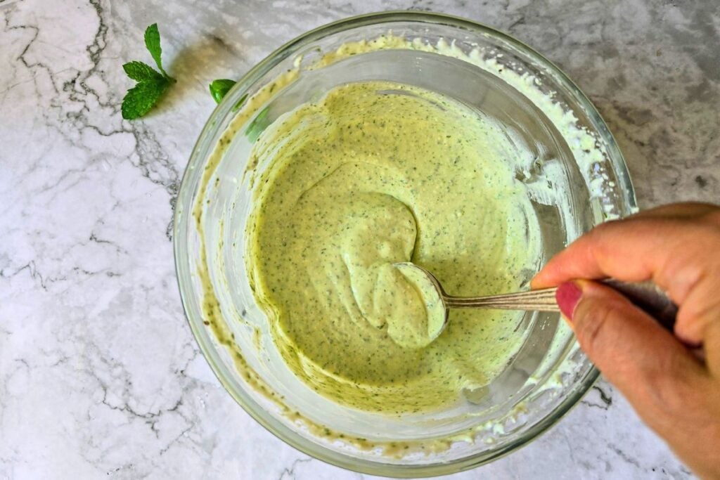 Whipped feta sauce with Greek yogurt, basil, and mint being stirred in a glass bowl