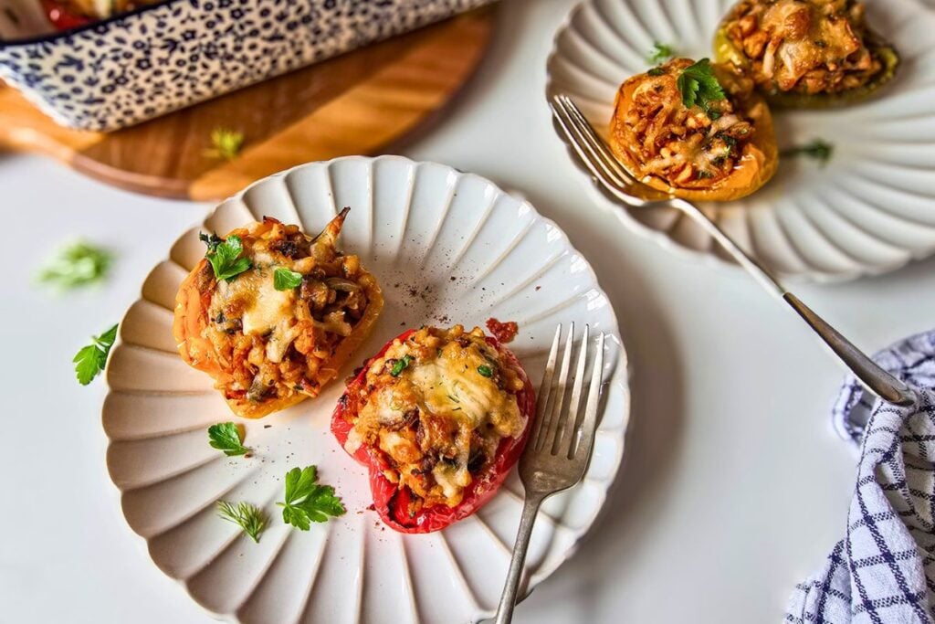 Barley stuffed peppers served on plates with forks, baking dish visible in the background.