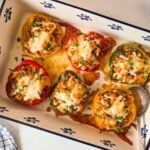 barley stuffed peppers in a blue and white baking dish, topped with melted cheese and fresh herbs.