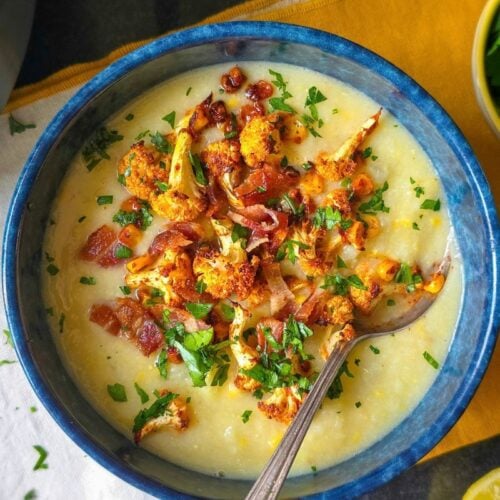 Cauliflower and corn chowder in a blue bowl with a spoon, topped with roasted cauliflower and corn.