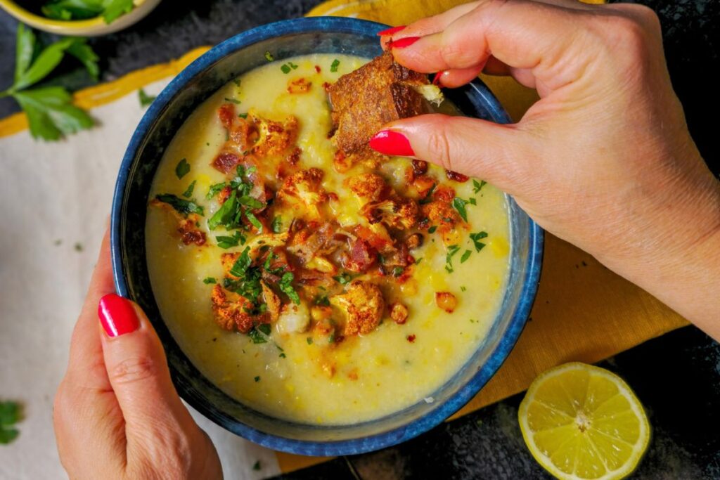 Dipping a slice of crusty sourdough into a bowl of cauliflower and corn chowder.