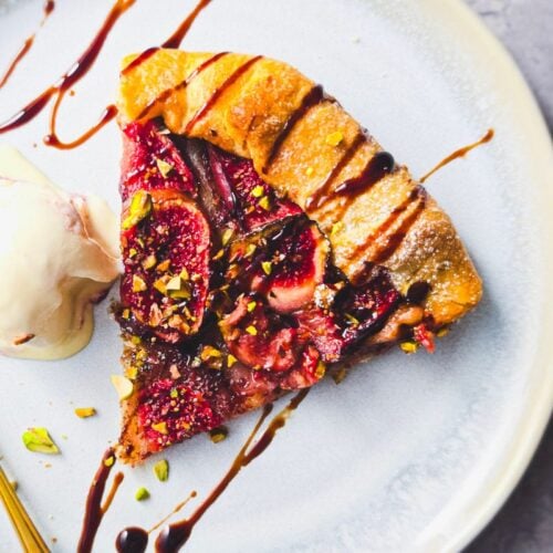 Slice of fig galette with chopped pistachios and balsamic glaze, served with a scoop of ice cream and a gold spoon
