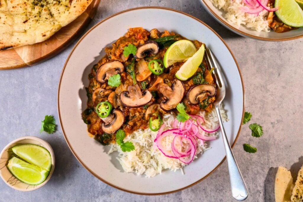 Mushroom and spinach curry served with basmati rice, pickled red onions, lime wedges and torn naan.