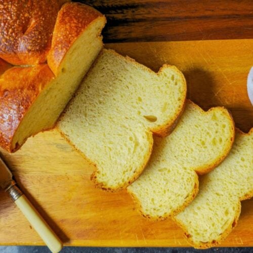 Sourdough brioche bread sliced on a wooden board, showing the golden crust and soft yellow crumb, with a small pot of jam