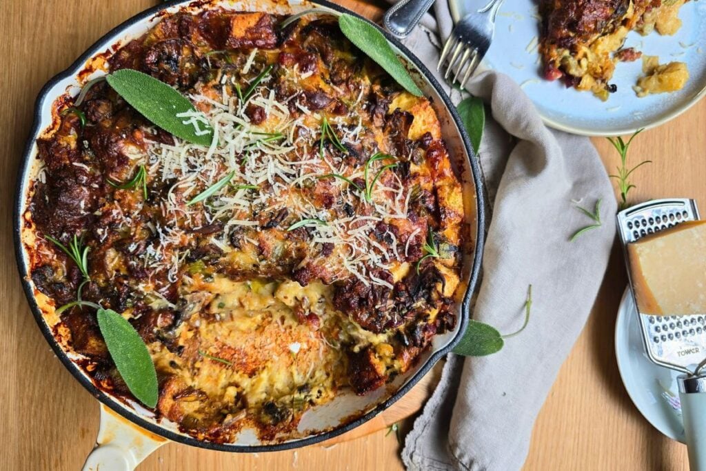 Cheesy breakfast strata in a skillet, topped with grated Parmesan and sage leaves made with leftover sourdough brioche