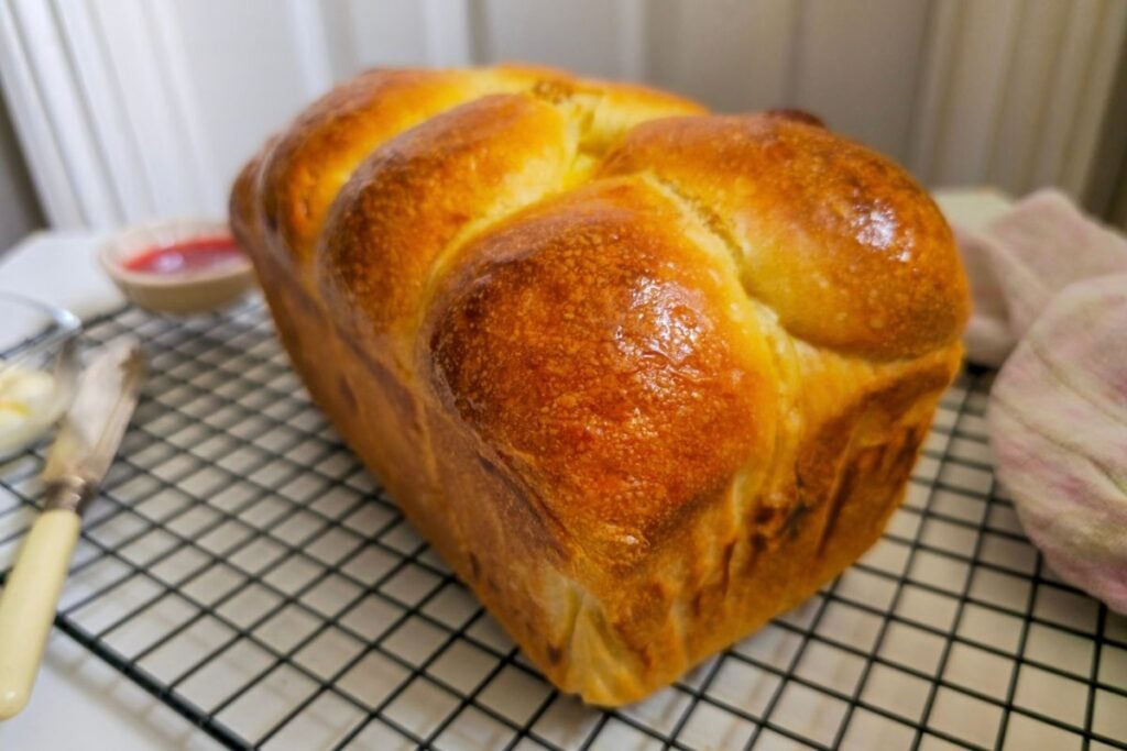 Whole sourdough brioche loaf with a glossy, deep golden crust cooling on a wire rack