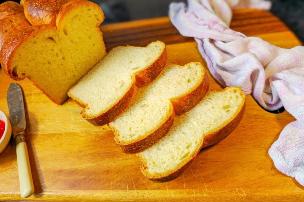 Angled view of sourdough brioche slices on a wooden board next to the tall loaf with its rounded, bumpy top