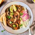 Bowl of creamy red lentil curry with browned mushrooms, spinach, cilantro and pickled red onions on rice.