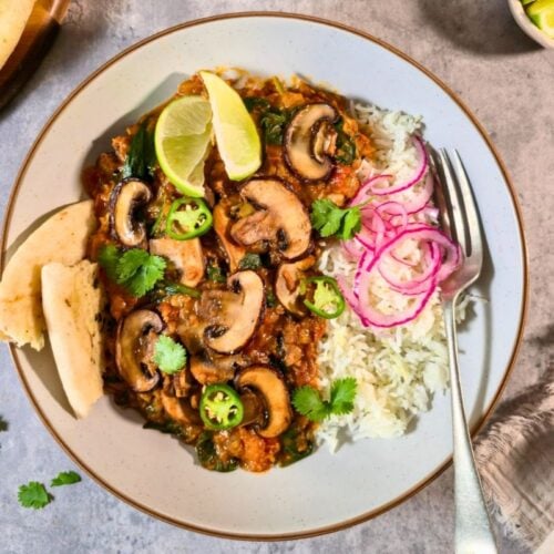 Bowl of creamy red lentil curry with browned mushrooms, spinach, cilantro and pickled red onions on rice.